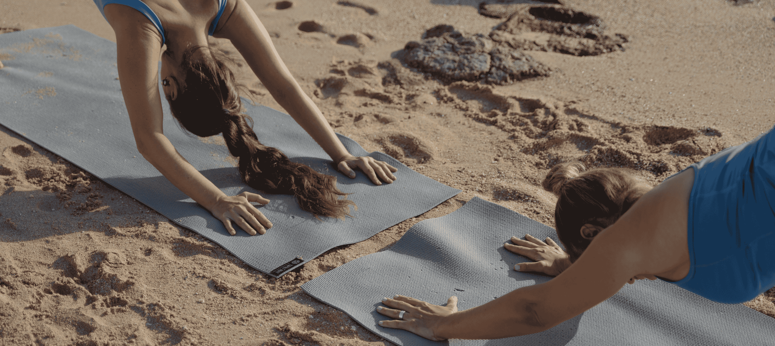 Two women doing yoga on sand