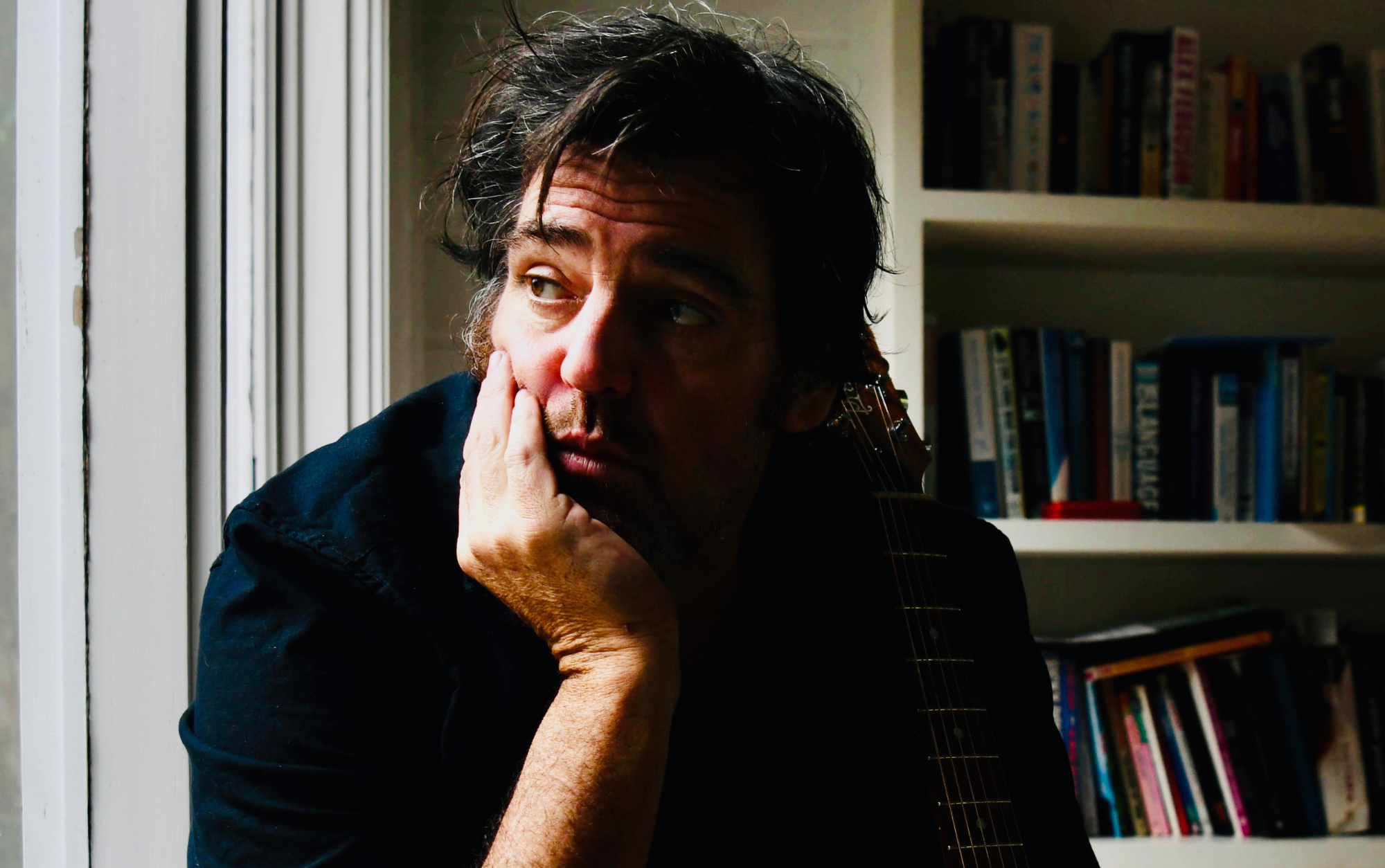 Alex Lloyd sitting with his guitar leaning on him