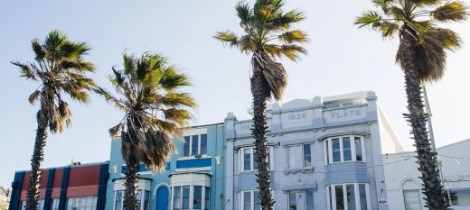 A photograph of a row of blue art deco buildings with palm trees in front.