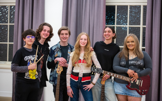 A multi gendered band with bright smiled in front of curtains