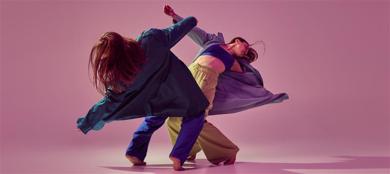 Two dancers on stage against a pink background