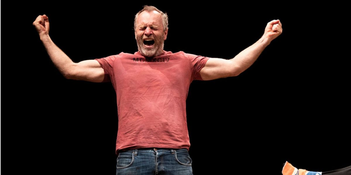 Man in red t-shirt on stage with arms raised up with eyes closed with a powerful expression on his face