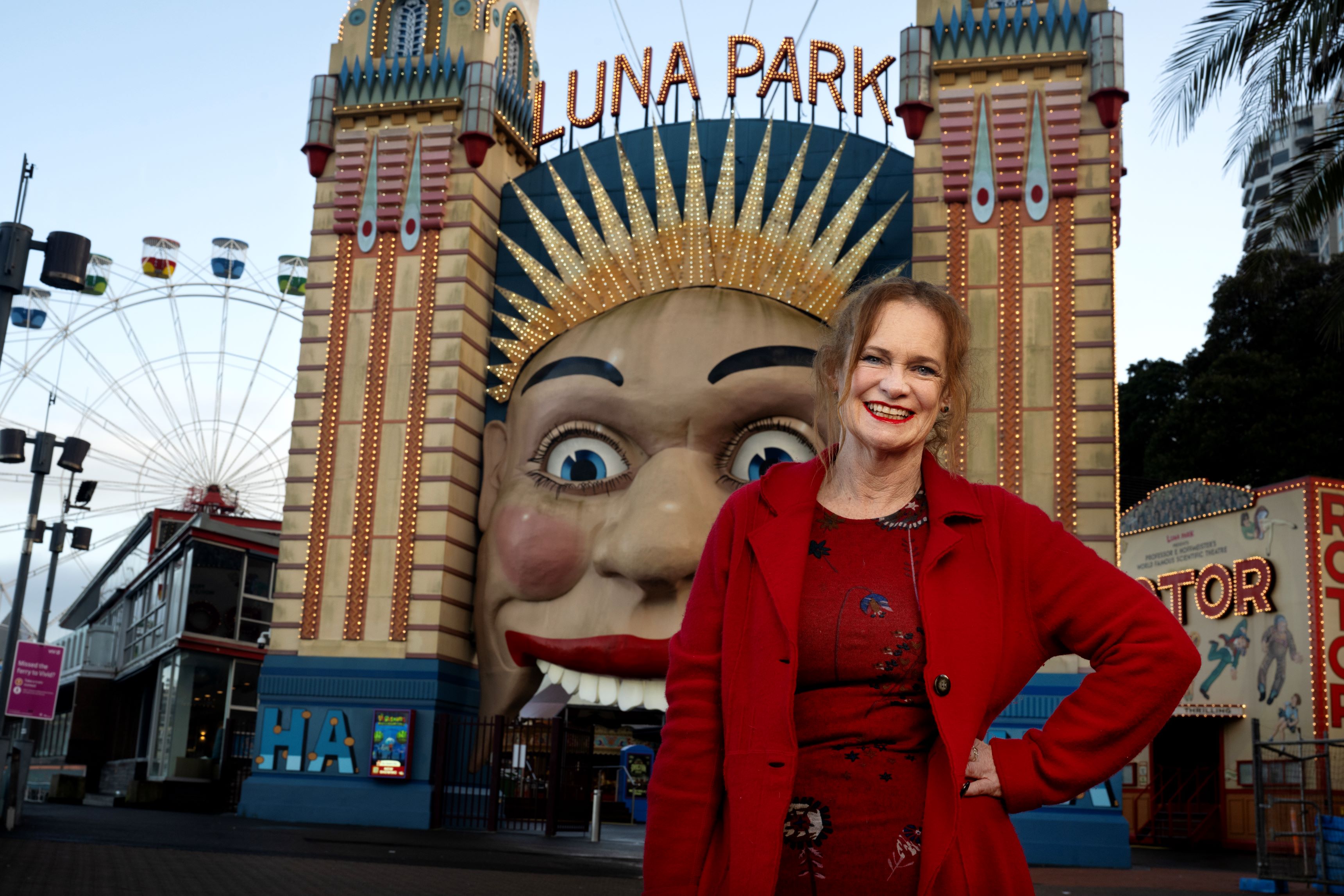 A woman with red hair and a warm smile stands in front of the iconic Luna Park frontage