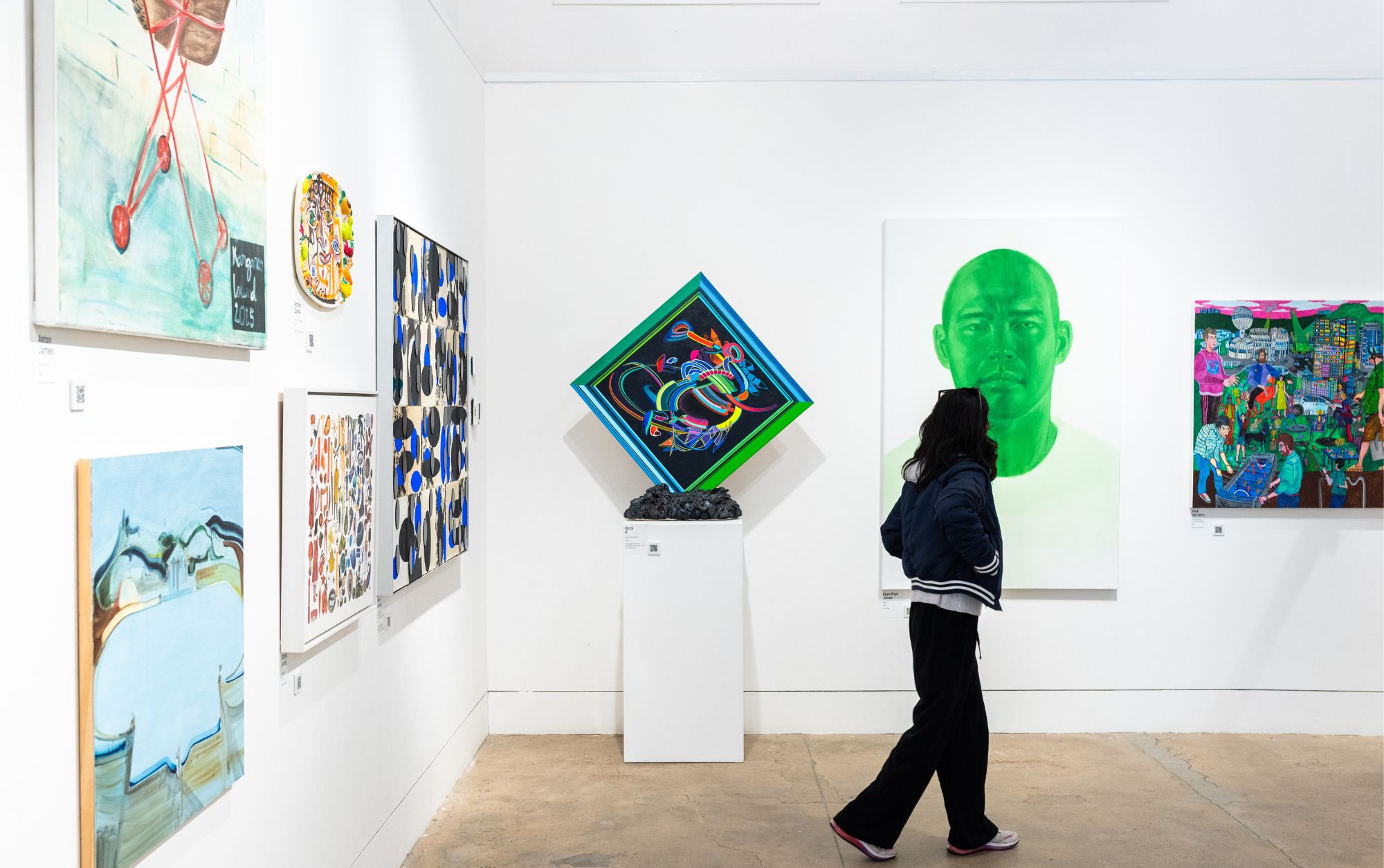 A person walks through a gallery with contemporary art on the walls and plinths.