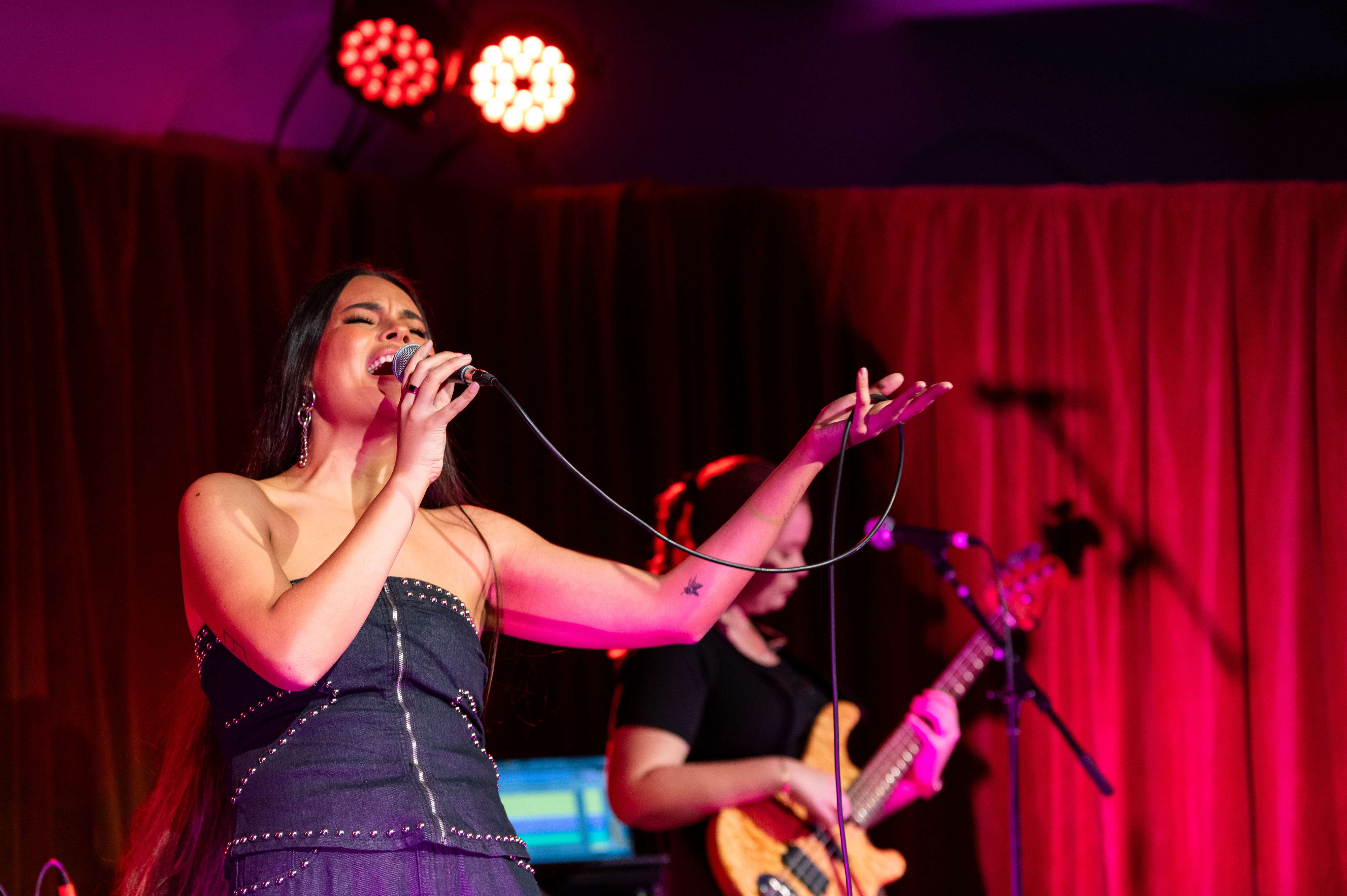 A First Nations woman with long hair sings on stage with warm lighting