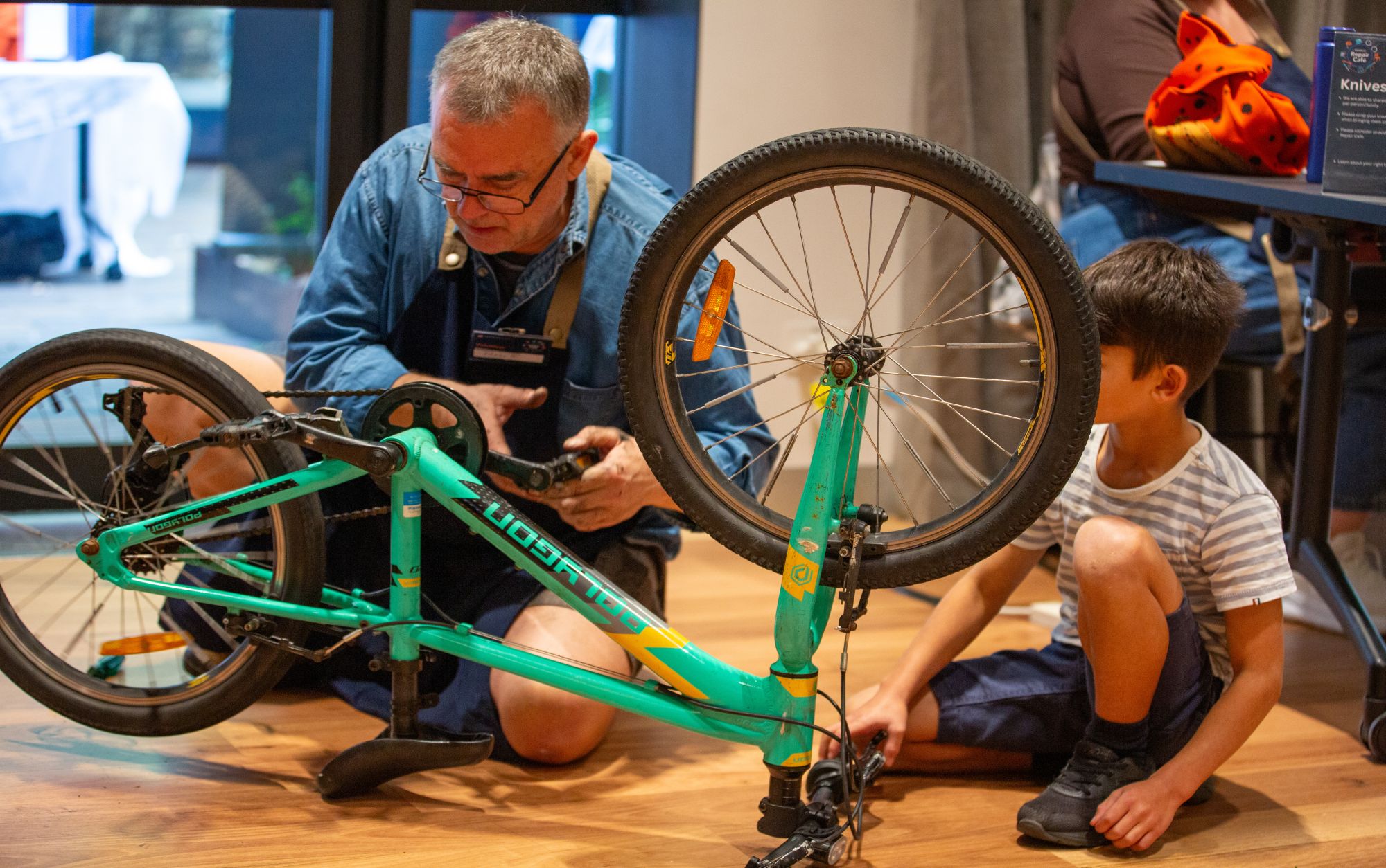 Man repairing a green bike whilst a boy is looking