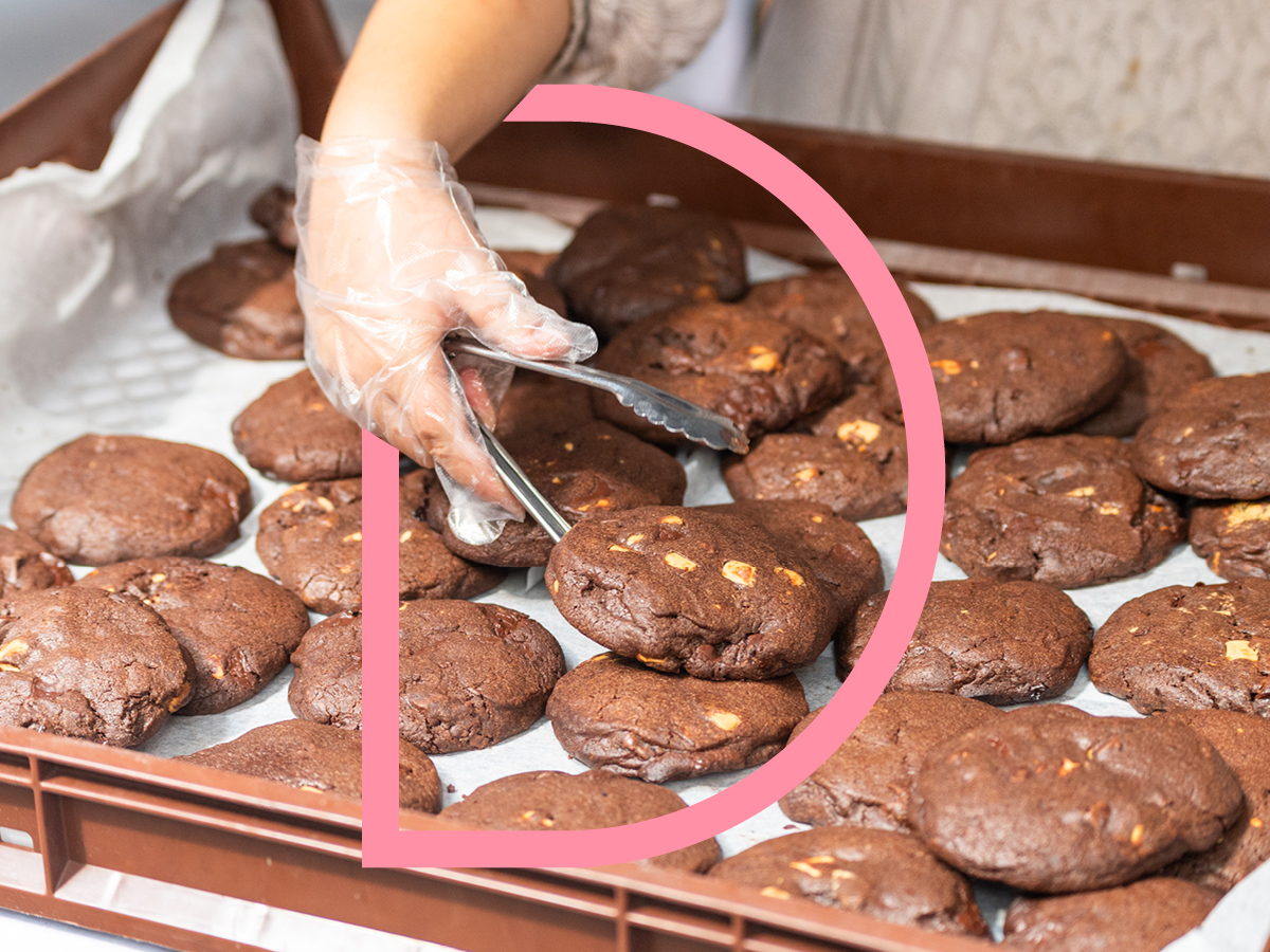 A hand reaches to scoop up chocolate cookies at a market stall