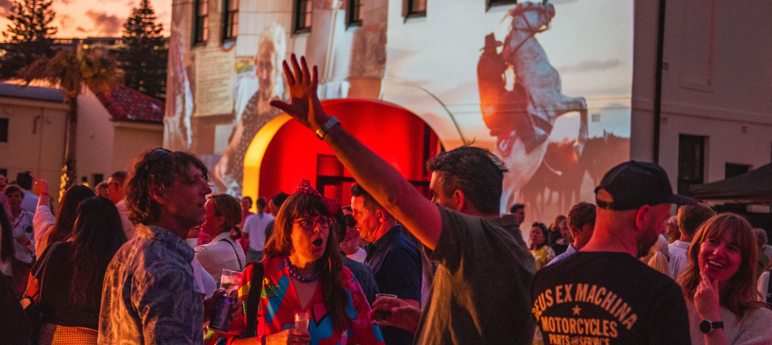 Image projects on Pav's gatehouse at night with people mingling in the background