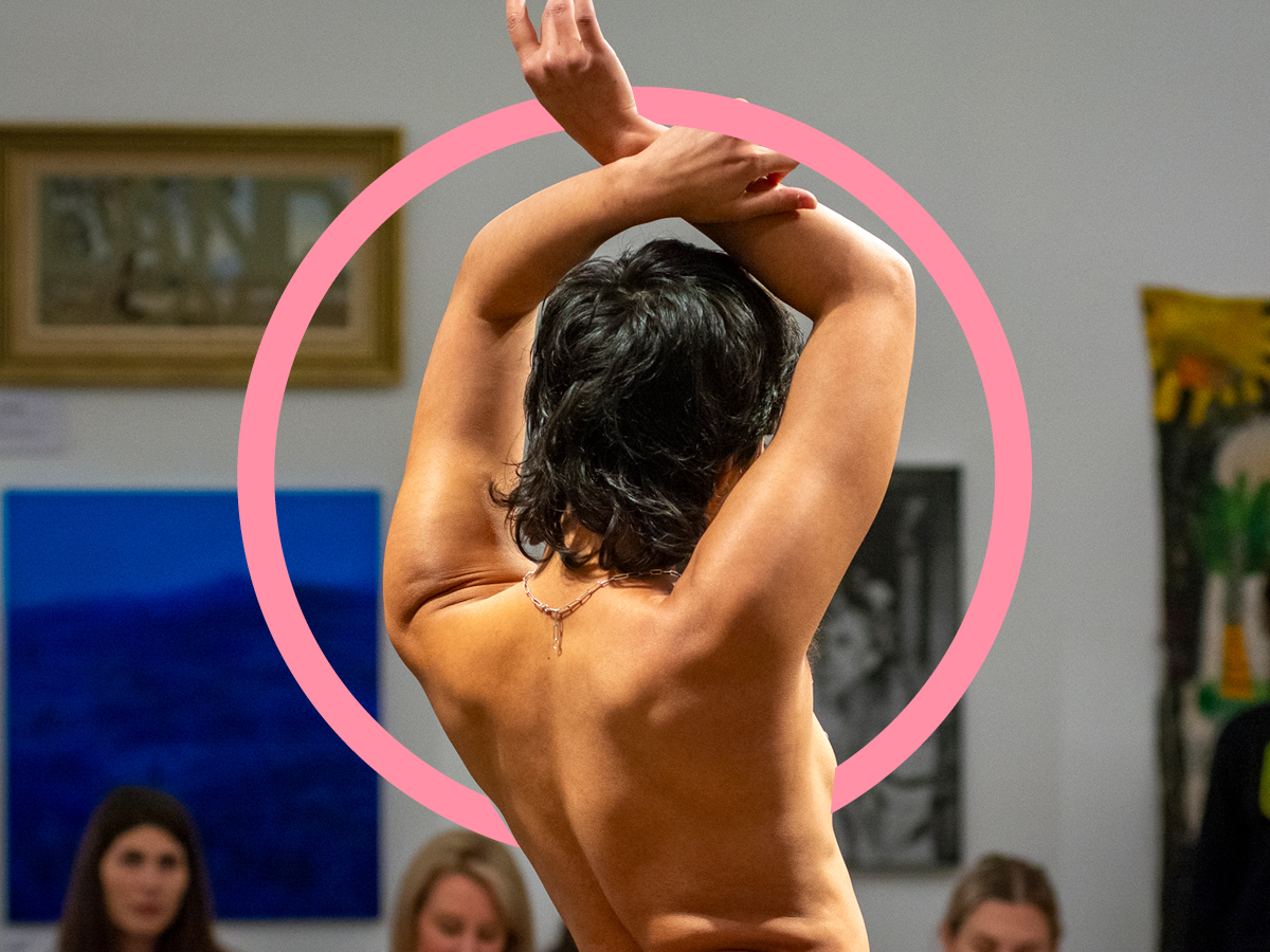 A nude model faces away from the camera at a live drawing class