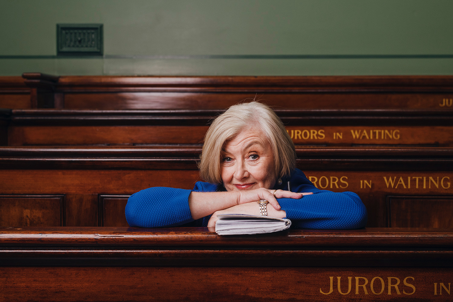 A woman with a sharp grey bob leans on a wooden chair