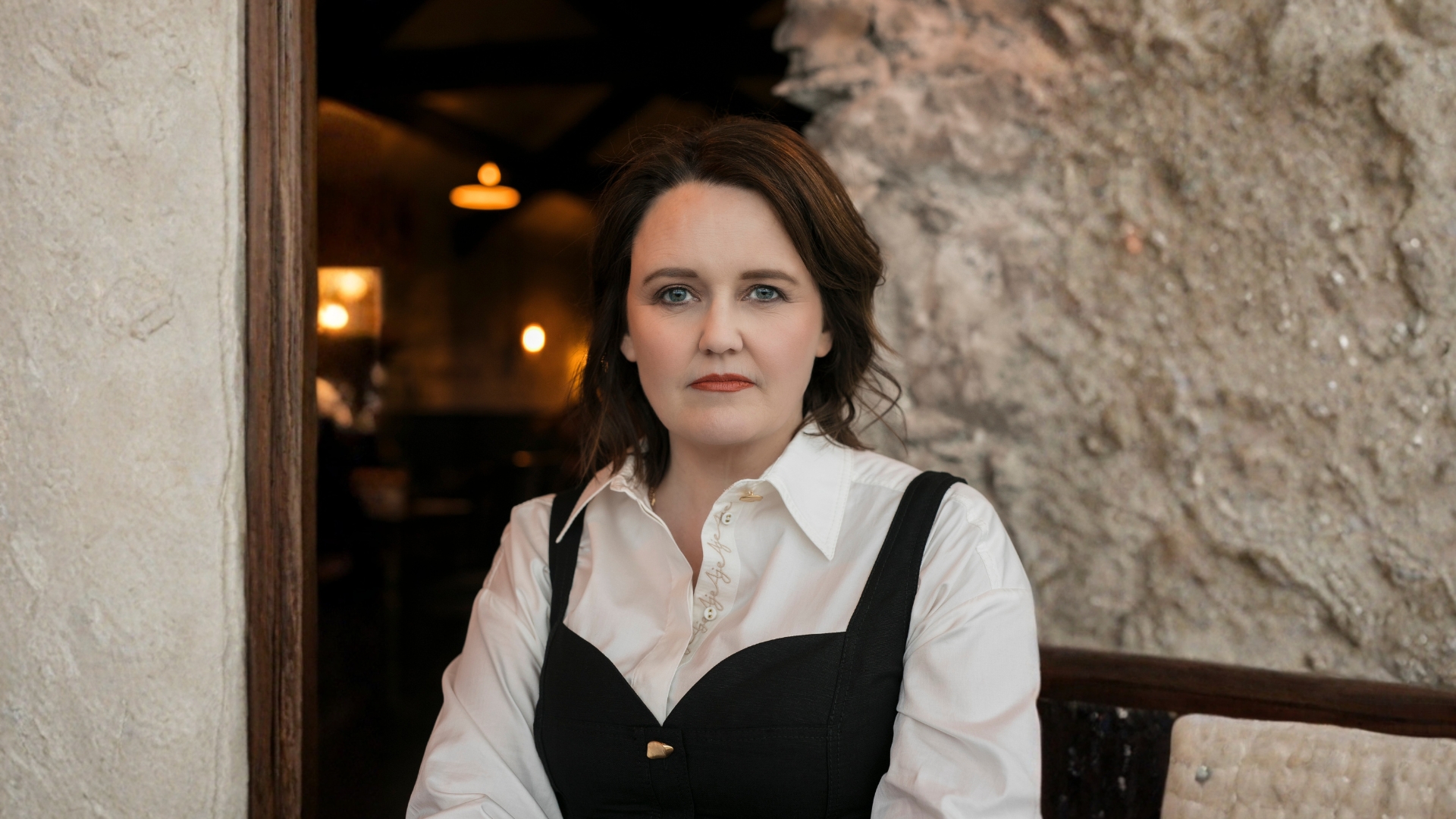 Author Dervla McTiernan an Irish Australian woman with dark long hair looks into the camera. She is wearing a black dress over a white collared shirt.