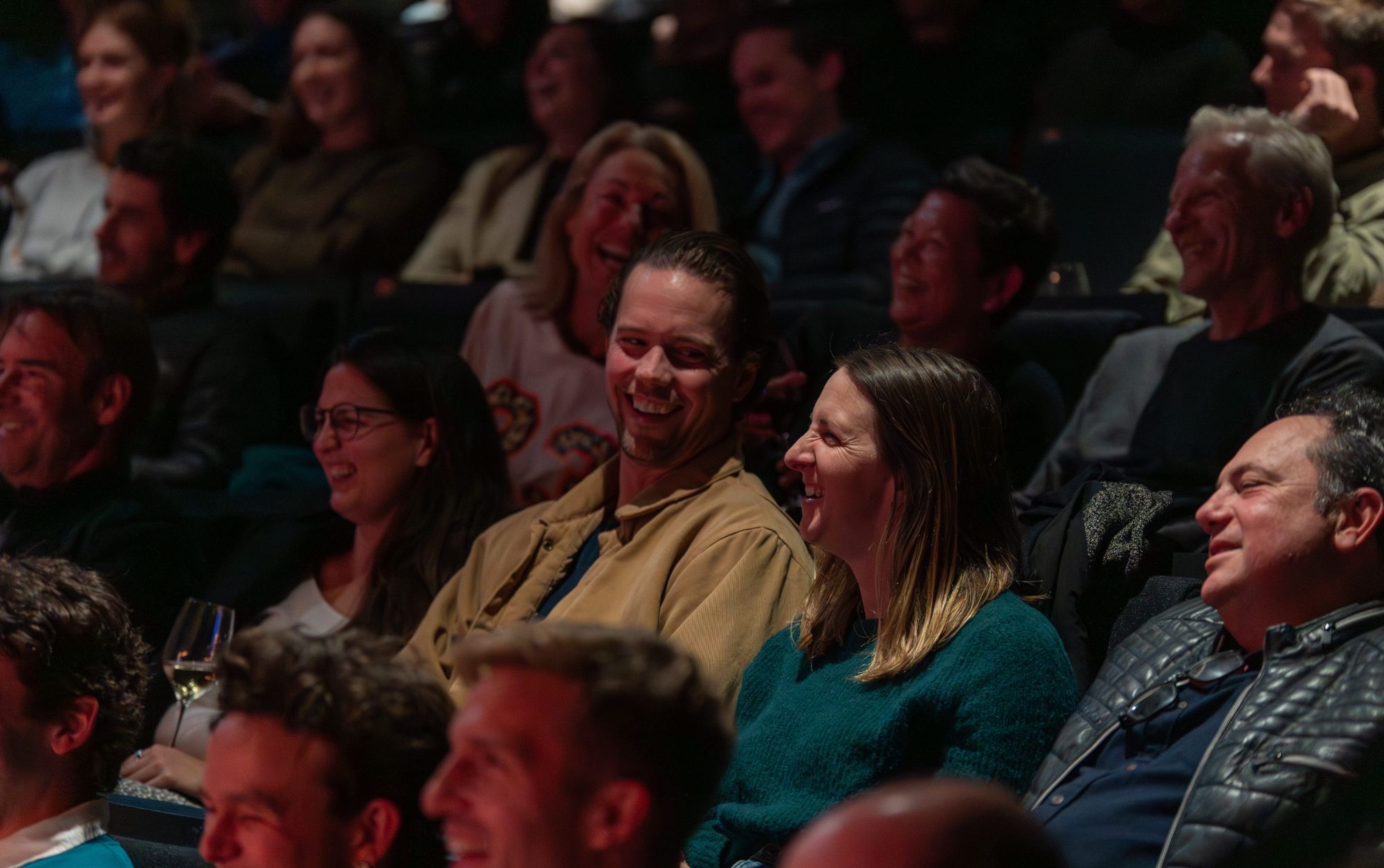 A seated audience of people are laughing, a man and woman are in focus. Photo by Lucy Parakhina
