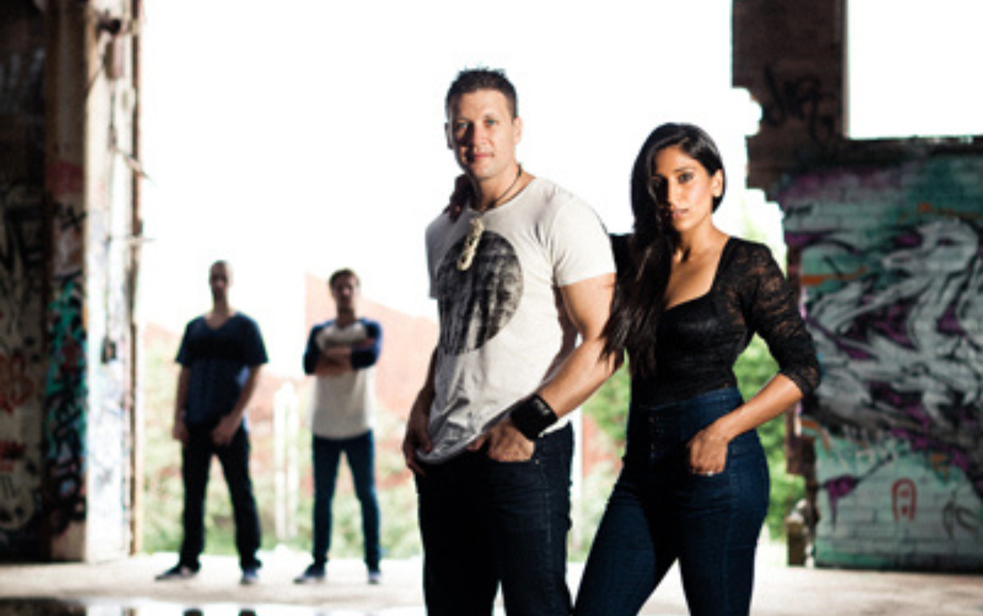 A male and female singers standing in foreground with band in background in a warehouse