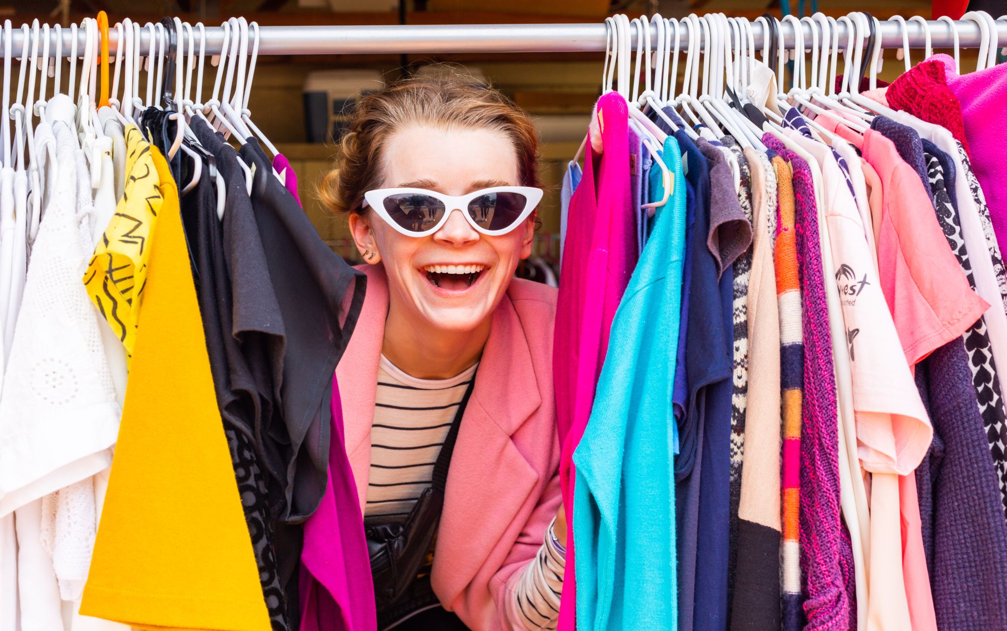 Woman between clothes hanging on a rack looking at the camera