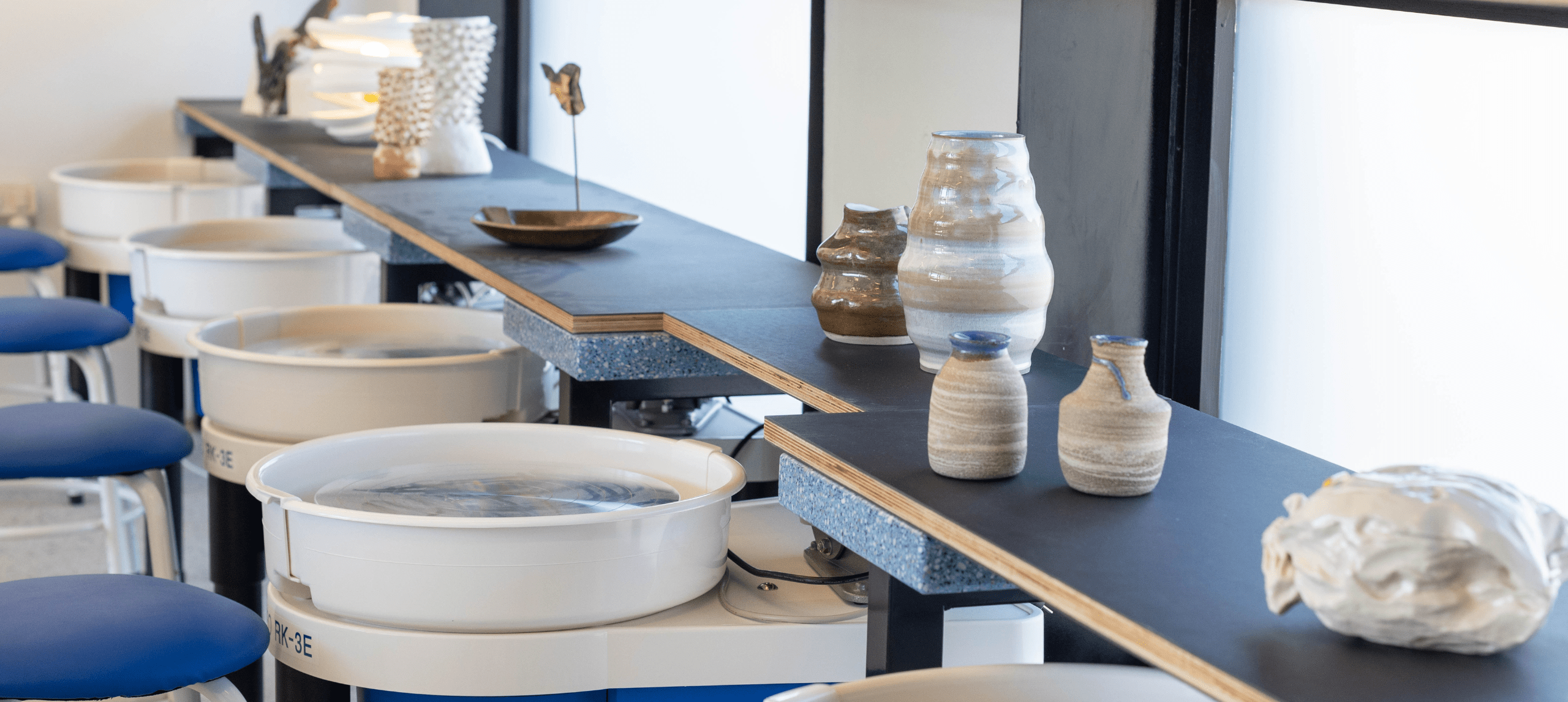 blue pottery wheels and clay sculptures in front of light filled arches in the pav's pottery studio