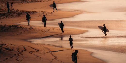 Surfers moving along a sunset beach