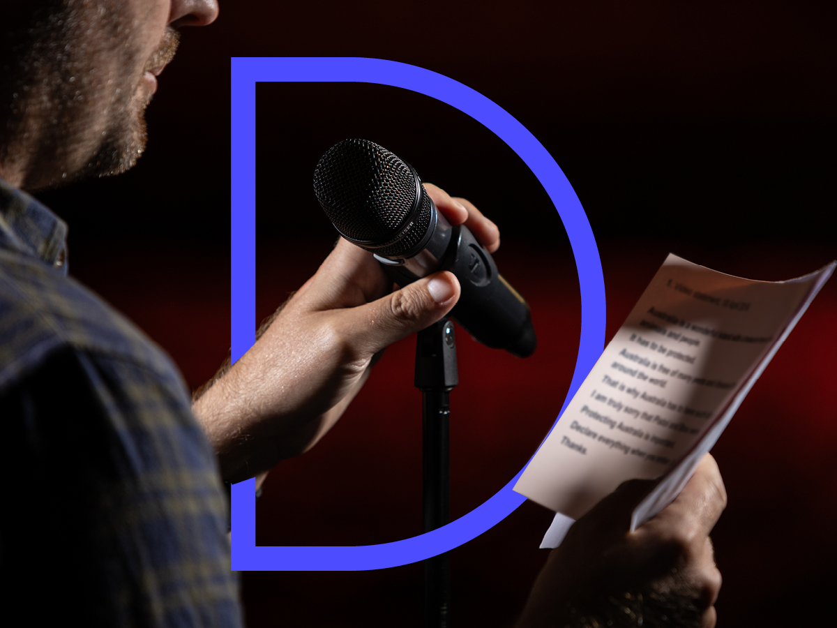 An unseen person holds a microphone and reads from a piece of paper