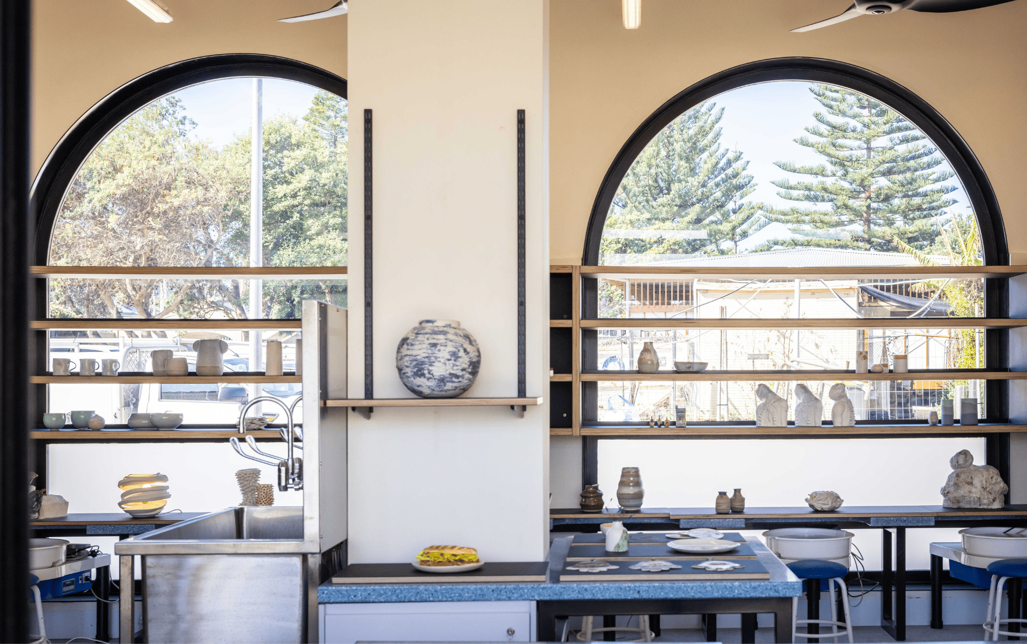 blue pottery wheels in the pav's studio in front of the light filled arches with pottery displayed on shelves