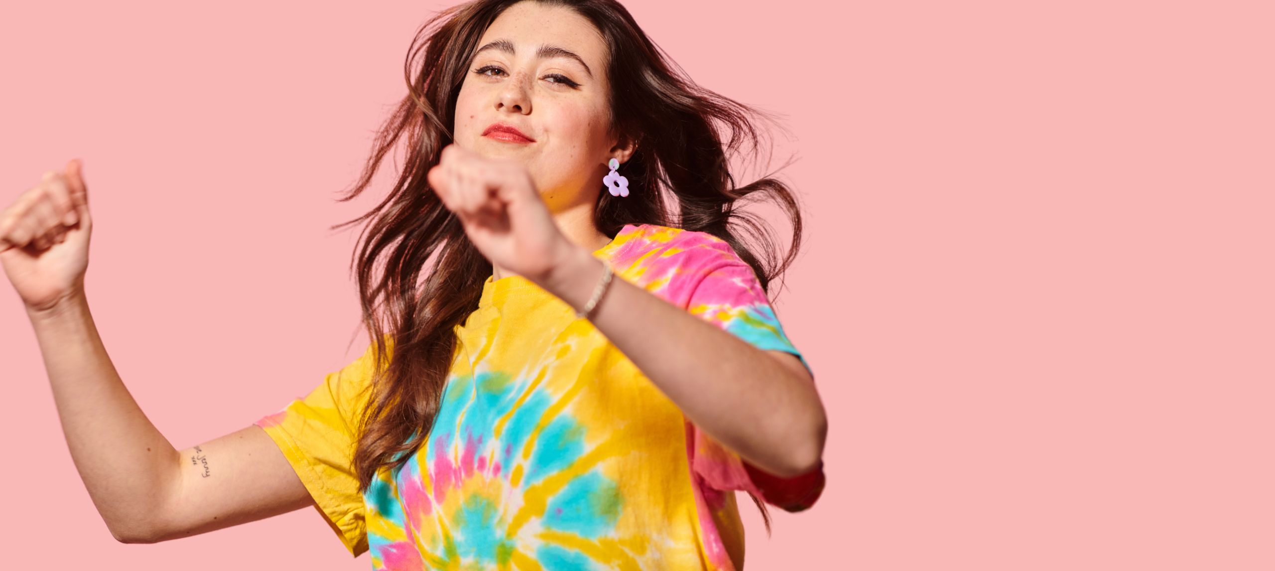young girl dancing in tie dye shirt with pink background