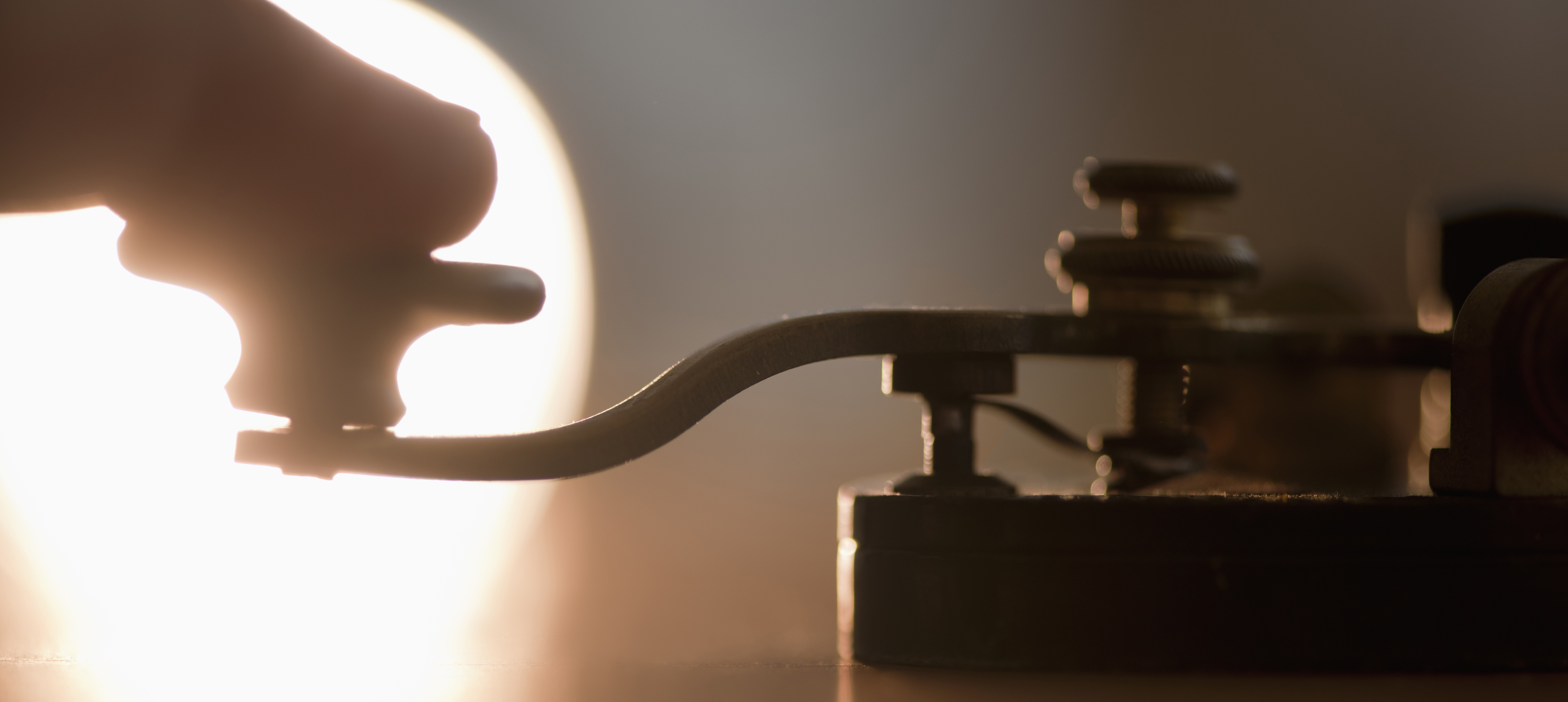 A shadowy backlit image of a finger tapping on a morse code device. 