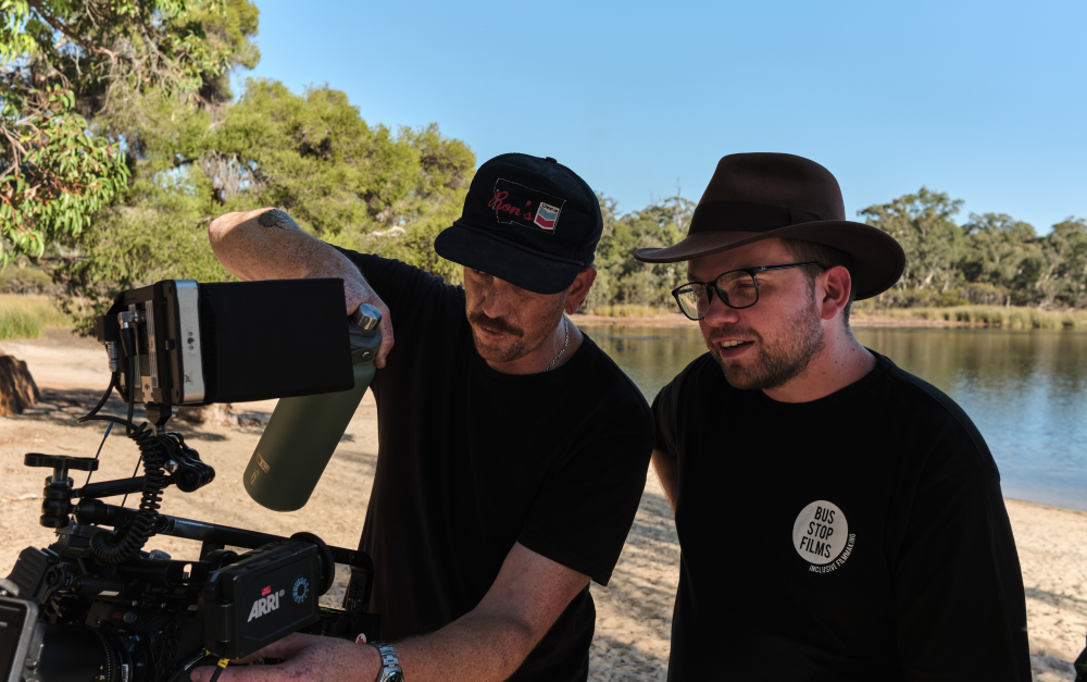 Student operating a video camera outside by a lake with a male student beside him